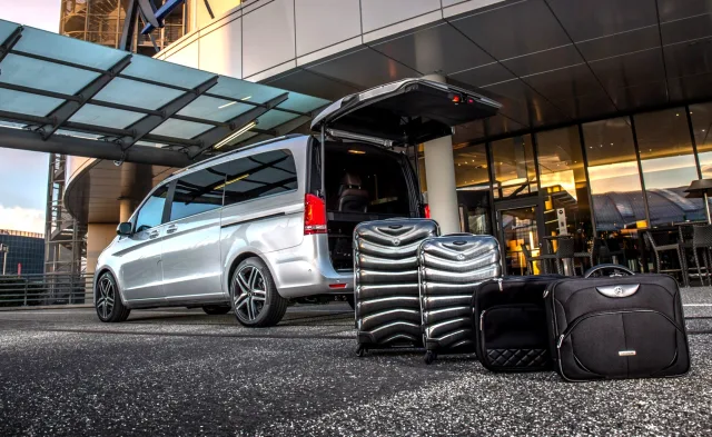 Mercedes van with the tailgate open and suitcases beside it at a venue entrance